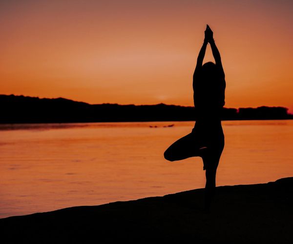Silhouette of a person in a yoga balance pose against a sunset.